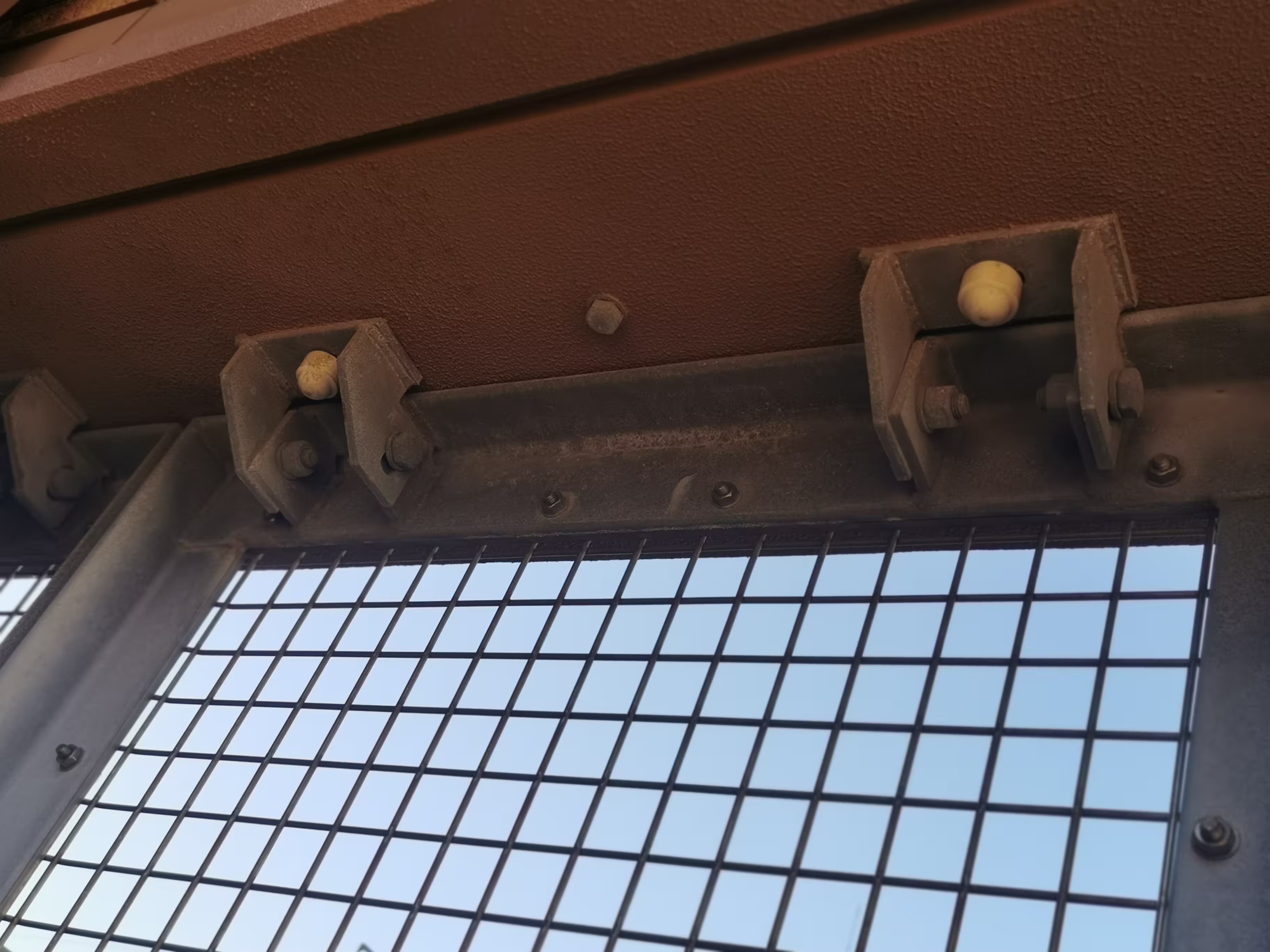 Detalle de fijación superior con escuadra y tornillería en rejilla de seguridad industrial